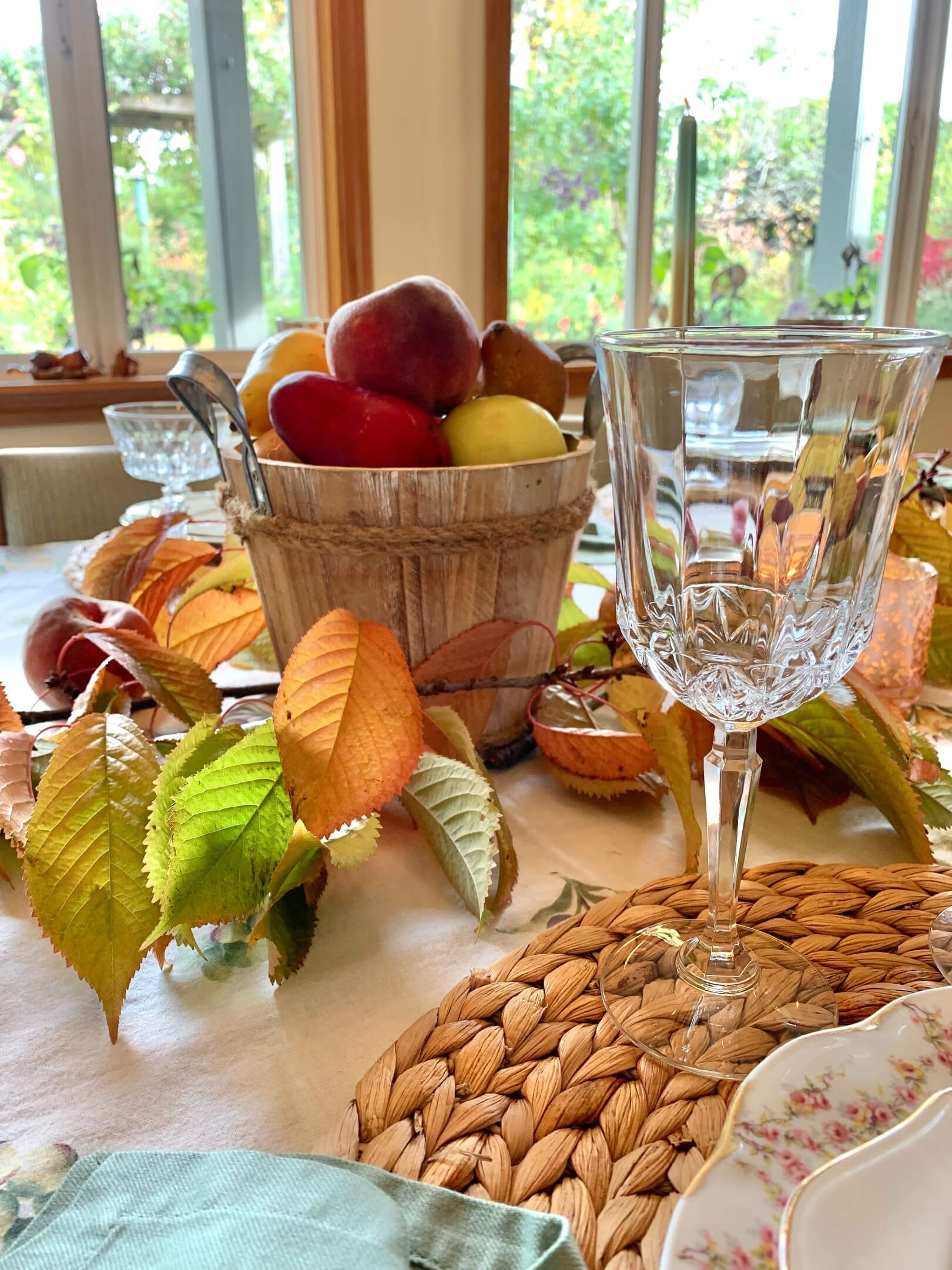 Autumnal table set up with wicker placemats, clear glassware with leaves and fruit for decoration