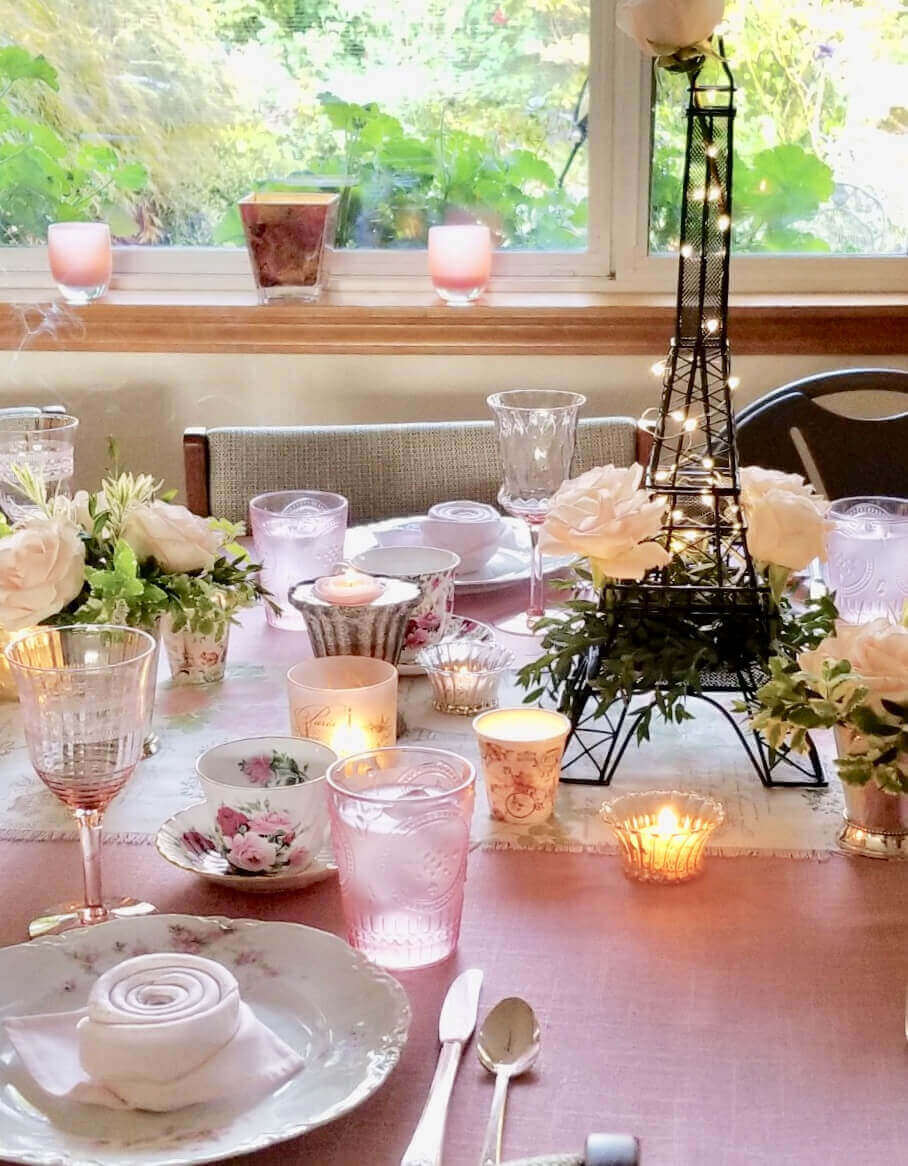 Paris and roses themed table set up, napkins shaped into rosebuds, Eiffel Tower shaped flower display, white crockery with pink floral patterns, a mixture of pink and clear glassware and white flowers for decoration