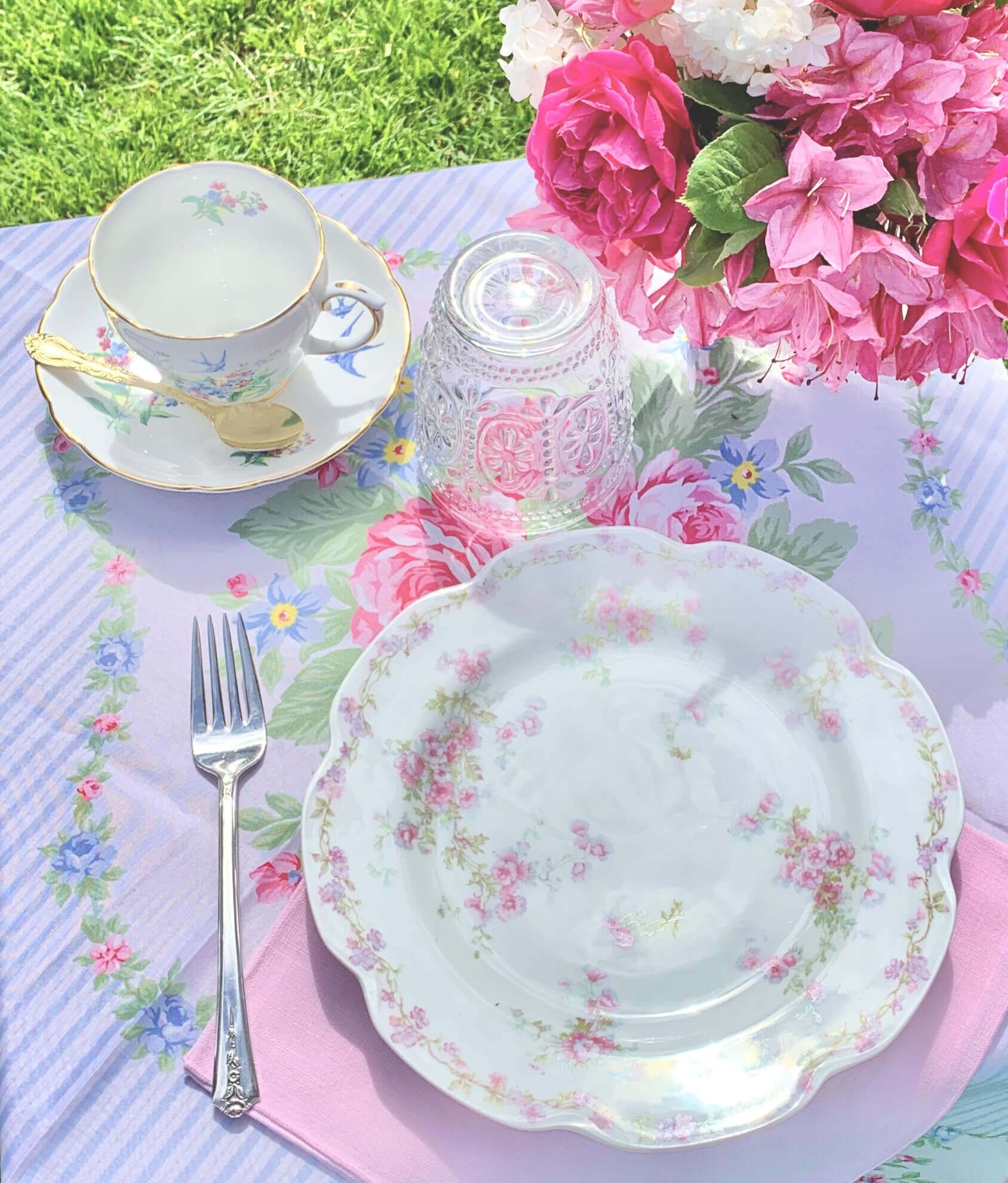 Blue and white striped tablecloth, pink floral crockery, teacup and saucer, clear glassware, pink floral decor