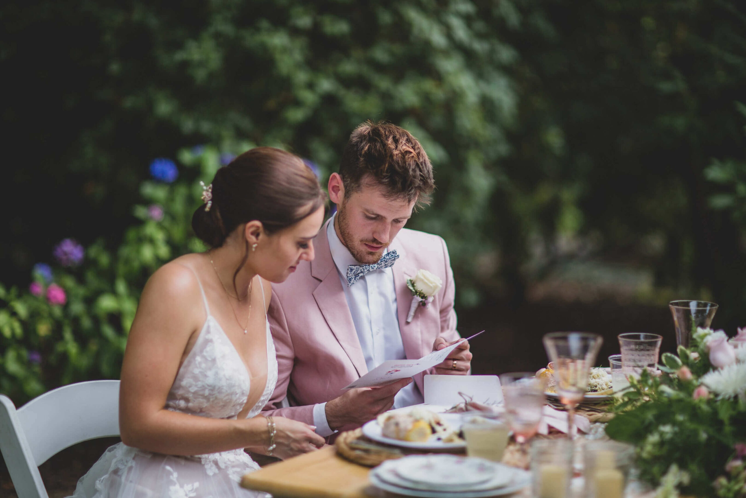 A bride and groom looking at their menu card at their sweetheart table. The table decor is a blush pink colour scheme with vintage white crockery rentals.