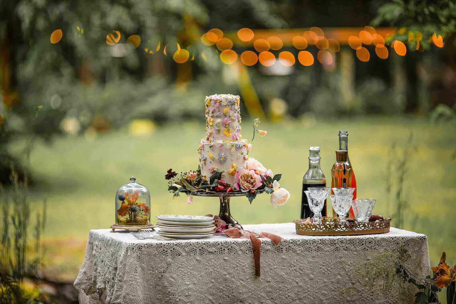 Vintage silver cake stand on an heirloom crochet tablecloth set up with a wedding cake, serving plates, clear glassware and drinks bottles
